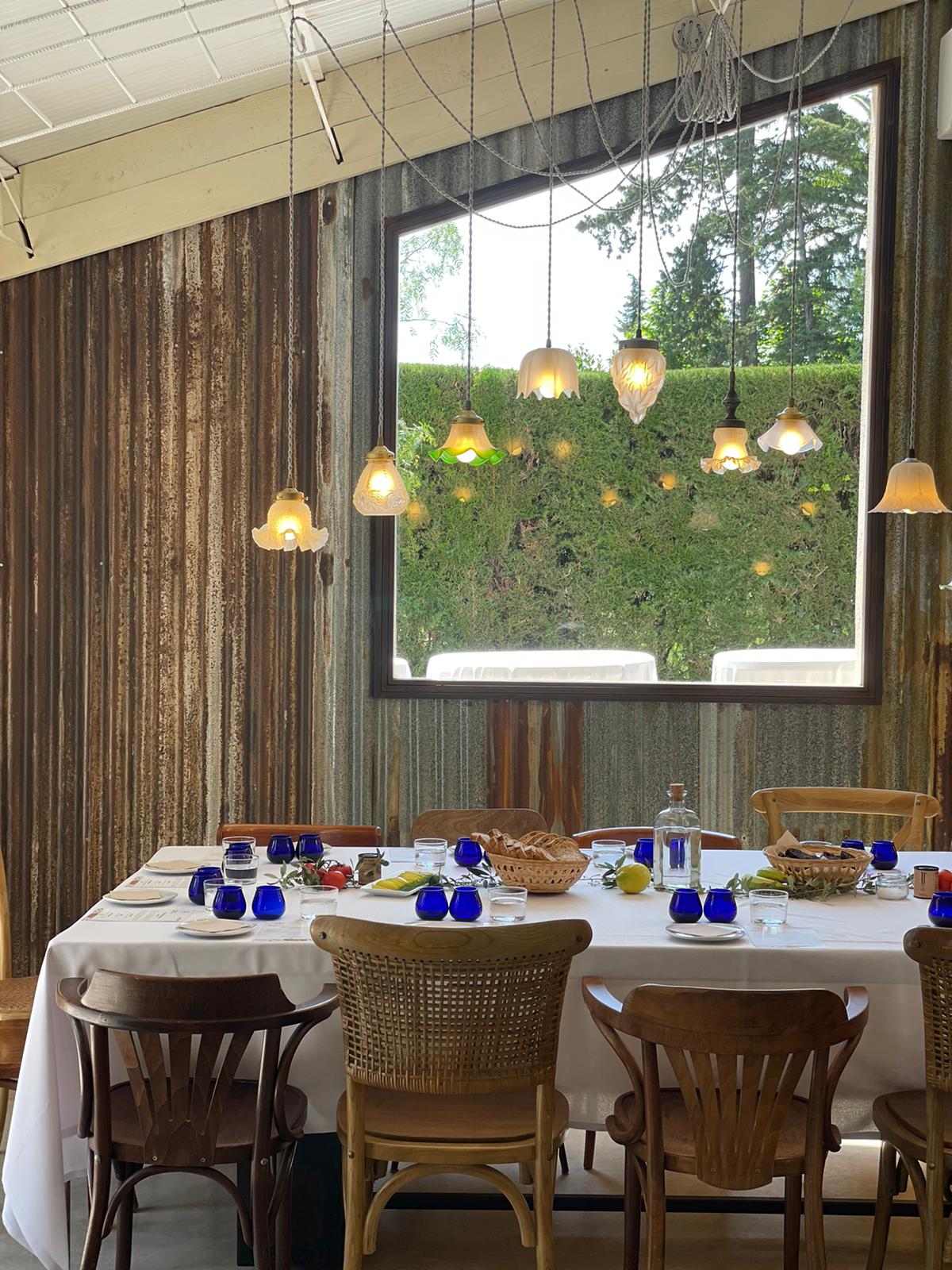 Foto de la sala de catas en la que se ve la mesa puesta, con los vasos oficiales para Cata de Aceite, las tulipas que iluminan la mesa y la ventana con vista a los jardines